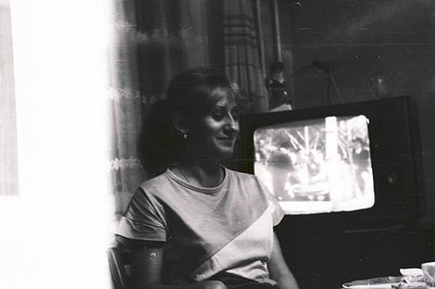 Woman seated, watching television in a dimly lit room. 1970s style furniture and a large, wood-grain television suggest the e...