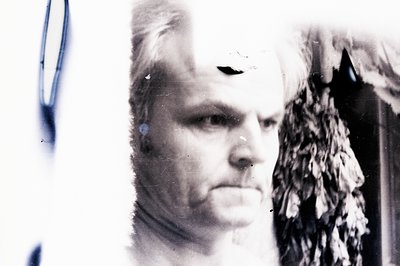 A close-up, black and white portrait of a man with short, styled hair and prominent facial features. The image shows signs of...