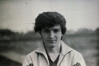 Formal portrait of a young man with dark, textured hair and a layered white shirt over a dark top. Natural, slightly blurred ...