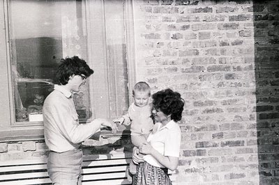 A candid family portrait showing a young boy being handed a treat by a man in bell-bottoms, while a woman holds him close nea...