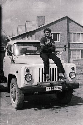 A young man in a striped shirt sits atop a vintage Soviet-era truck, likely a UAZ-452. The vehicle's license plate reads "432...