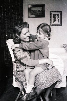 A mother and daughter share a loving embrace on a folding chair. The woman, dressed in a patterned dress, smiles warmly at he...