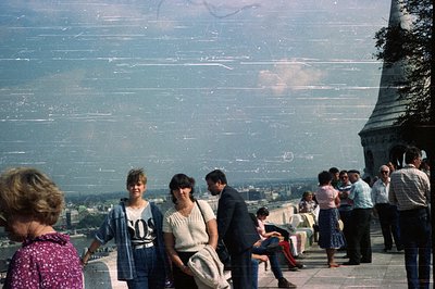 Crowded viewing platform, likely Paris, France. People observe a distant cityscape; the Eiffel Tower dominates the right fram...