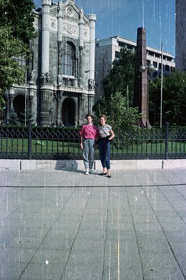Two young people stand before a grand, ornate building exhibiting neoclassical architecture. The building features multiple a...