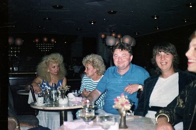 A social gathering at an upscale venue, likely a restaurant or private club. Four individuals are seated at a table featuring...