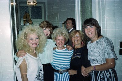 Group portrait of five people with voluminous hairstyles, characteristic of the late 1970s or early 1980s. A man stands parti...
