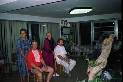Group portrait inside a mid-century modern home, possibly a vacation rental. Five individuals pose; floral wallpaper and larg...