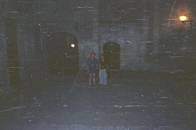 A couple walks along a cobblestone pathway within an ancient stone structure. Visible architecture includes arched doorways &...