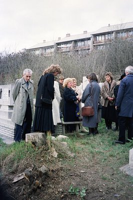 Group of people appears to be participating in a formal gathering, possibly a tour or memorial, in front of a brutalist-style...