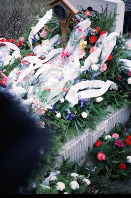 A memorial service or funeral arrangement features vibrant floral displays and white ribbon decorations on a stone structure....