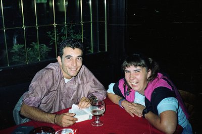 Two young adults seated at a table covered with a vibrant red tablecloth smile for the camera. A glass of beer sits on the ta...