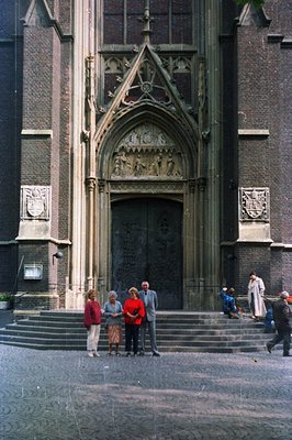 Monumental Gothic architecture features an ornate doorway framed by detailed stone carvings. Three figures stand on the steps...