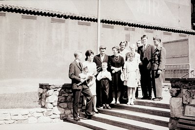 Group portrait showing a man in a suit holding a baby, standing on a stone staircase alongside other adults and children. Lik...