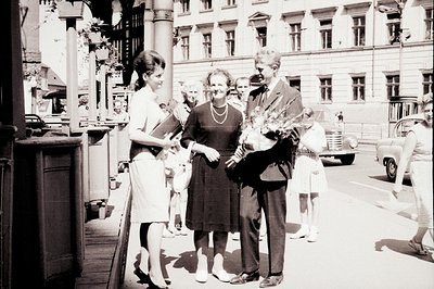 A formally-dressed couple are presented with flowers by a woman in a modest dress. Two young girls in party dresses flank the...