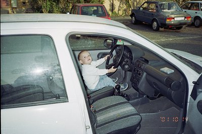 A young boy sits in the driver's seat of a white Volkswagen, playfully gripping the steering wheel. Visible date stamp indica...