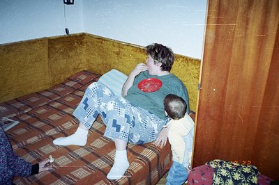 A boy in patterned pajama pants and socks lounges on a patterned bedspread in a room with distinctive orange shag carpeting a...