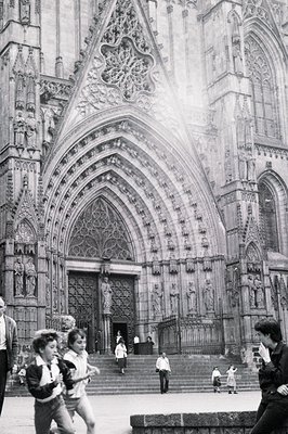 Monumental view of a Gothic cathedral façade, likely Notre Dame, showcasing intricate carvings & a rose window. Several peopl...