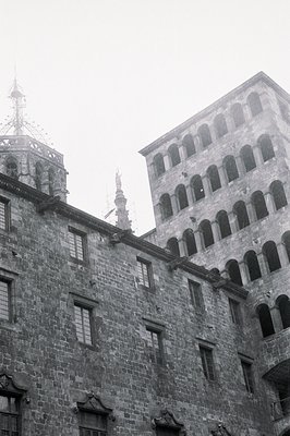 A low-angle, black and white image depicts a portion of a medieval stone building, likely a palace or fortress. Note the tier...