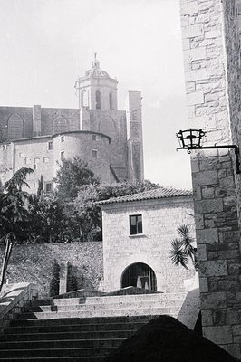 A stone building with an arched opening and single window fronts a tiered landscape featuring a large, historic structure wit...