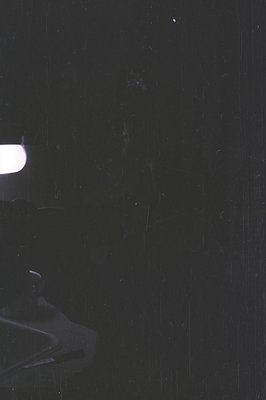 Black and white photograph featuring a partially visible vintage turntable. The record sits on the platter, illuminated by a ...