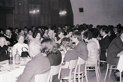 A large crowd gathered at a formal event, likely a banquet or conference. Guests are seated at tables, dressed in 1970s attir...