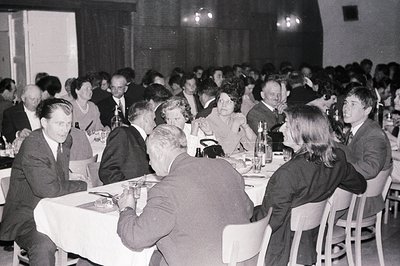 A formal gathering, likely a banquet or business event. Numerous formally dressed attendees sit at tables covered with white ...