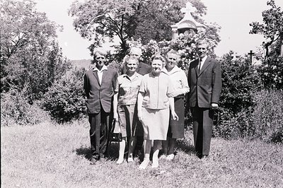 A formal portrait of five individuals, likely a family, posed in a grassy area with a small, ornate chapel visible in the bac...