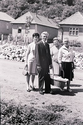 Family portrait from the 1960s or 70s, featuring a man in a suit, a young woman in a dress, and two older women carrying a pi...