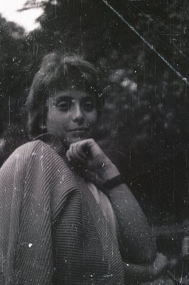 A young woman with short, layered hair poses outdoors, appearing relaxed. She wears a textured knit sweater and a dark wristw...