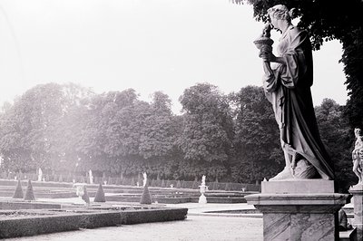 Formal French garden design with a classical statue. Tiered landscaping, manicured hedges, and fountains define a symmetrical...