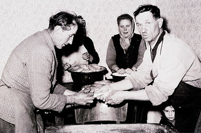 A family gathers around a large pot, seemingly making or preparing cheese. A man kneads dough while another gestures, possibl...