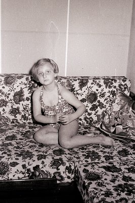 Young girl in a patterned swimsuit sits on a floral-patterned sectional sofa. Interior scene, likely a holiday accommodation....