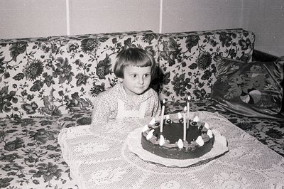 A young girl with short, dark hair sits behind a table adorned with a lace tablecloth, celebrating a birthday with a chocolat...