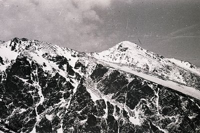 Dramatic, snow-covered peaks dominate the landscape. Stark contrast highlights a rugged alpine terrain with visible rock form...