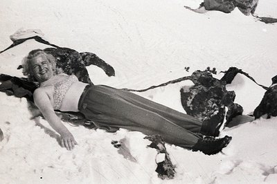 A smiling woman reclines in the snow, wearing a patterned bra top and wide-legged trousers. The image, likely taken in the 19...