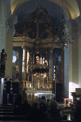 Ornate gilded altar dominates a church interior. A depiction of a figure is centered within, flanked by statues and elaborate...