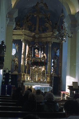 Ornate, gilded altar with religious statues and a central painting occupies the focal point within a blue-toned church interi...