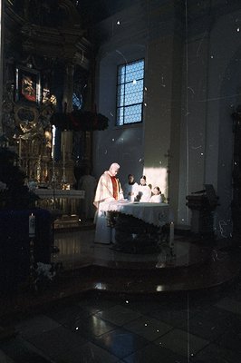 A solemn religious scene within a Catholic church. A priest in vestments presides over the altar, with acolytes nearby. Ornat...