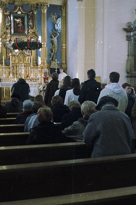 A formal religious service unfolds within a traditional Catholic church. Attendees are seated in pews, facing an ornate altar...
