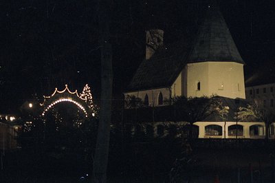 Night view of a stone building with a distinctive, domed tower and arched entrance decorated with string lights. Likely a Eur...
