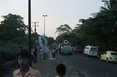 Street scene featuring a parade with a large decorated float, vehicles, and onlookers. Appears to be a rural town, possibly S...