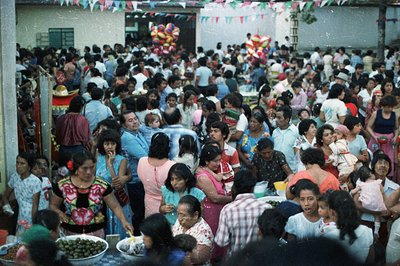 Crowded outdoor gathering, possibly a festival or community event. Numerous people of various ages are present, enjoying food...
