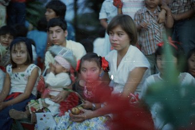 Group portrait shows children, likely in a rural setting. A young girl holds flowers, while a teen holds her hand. Garments s...