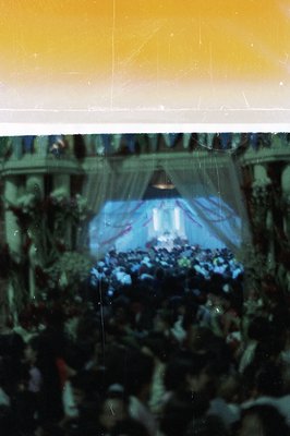 Large crowd gathered before an elaborately decorated stage with draped curtains and floral arrangements. The event appears to...