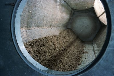 Close-up view within a dark, circular structure reveals layered sediment. Predominantly earthy browns and tans form a granula...