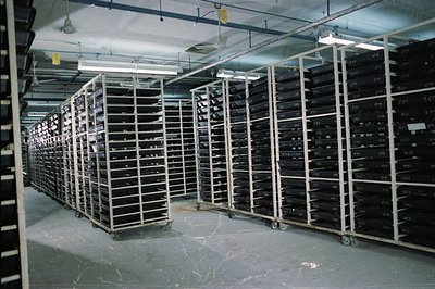 Expansive archival storage room features rows of white metal shelving carts densely packed with film canisters, likely negati...