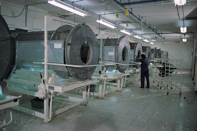 Industrial lab scene: multiple film processing tanks line a long room. A technician in dark clothing works alongside the mach...