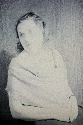 Portrait of a young woman, arms crossed, seated. Formal studio pose, likely 1920s-1930s. Detailed floral wallpaper in the bac...