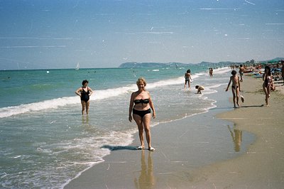 Seaside scene features a woman in a black swimsuit walking on a sandy beach, with a wider view of the coast and sea. Other be...