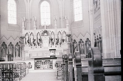 Interior view of a Catholic church, showcasing an ornate altar with statues, floral arrangements, and a crucifix. The archite...
